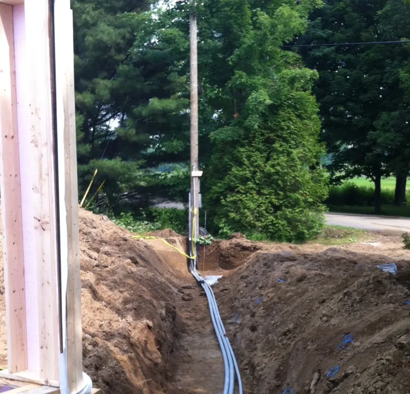 Overhead-to-underground service under construction: grey conduits along the pole, then in the trench to the house