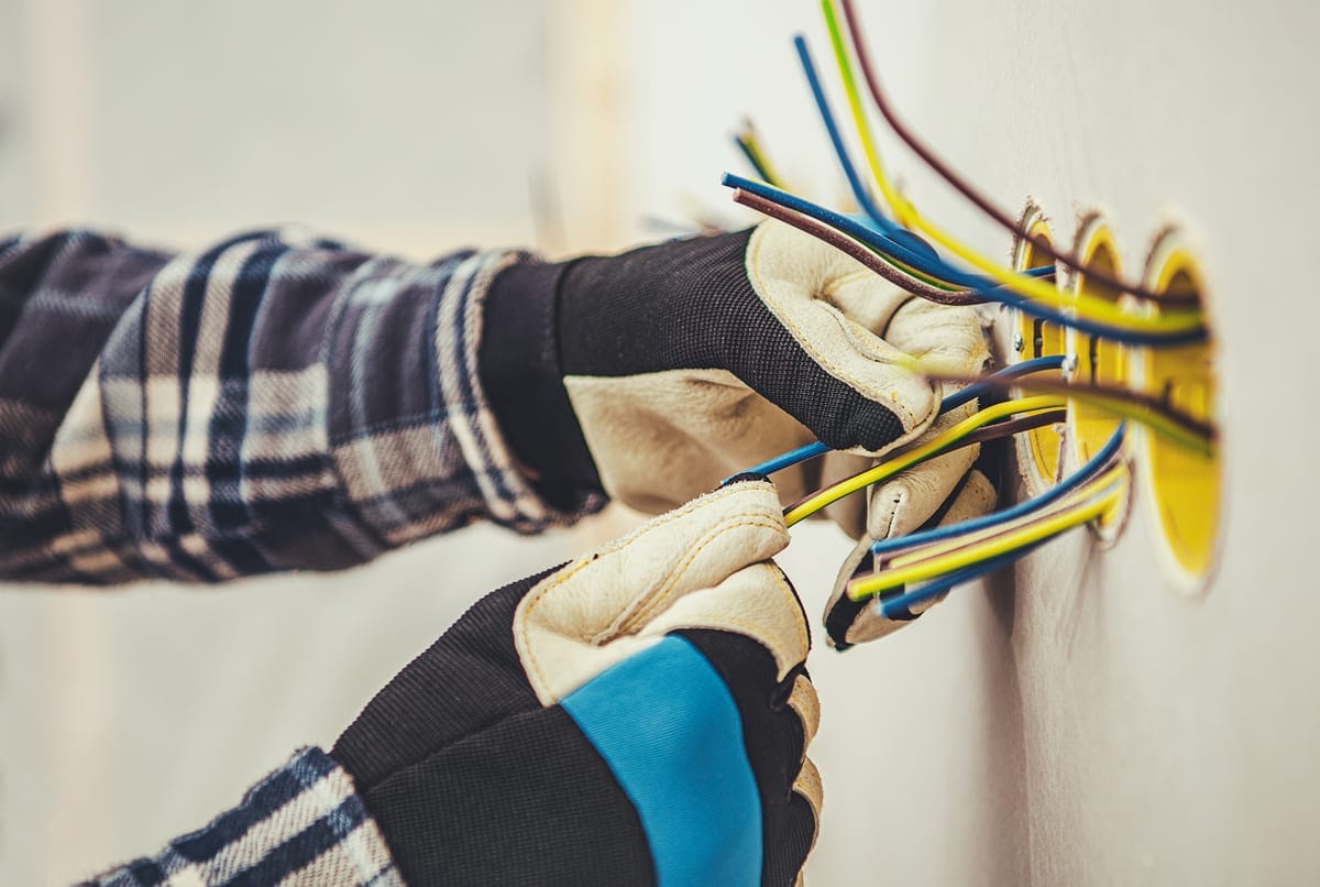 Mains gantées d'un électricien raccordant des fils de couleur dans une boîte murale